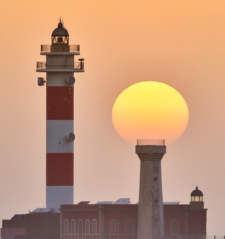 A setting sun lined up behind a lighthouse